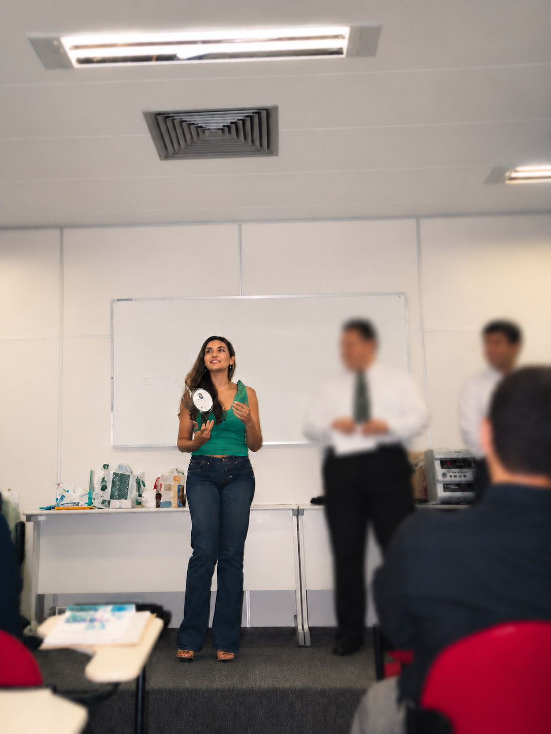 Eliane Pessin no início da carreira, apresentando em uma sala de aula e segurando um prêmio; as pessoas ao lado aparecem com o rosto desfocado.